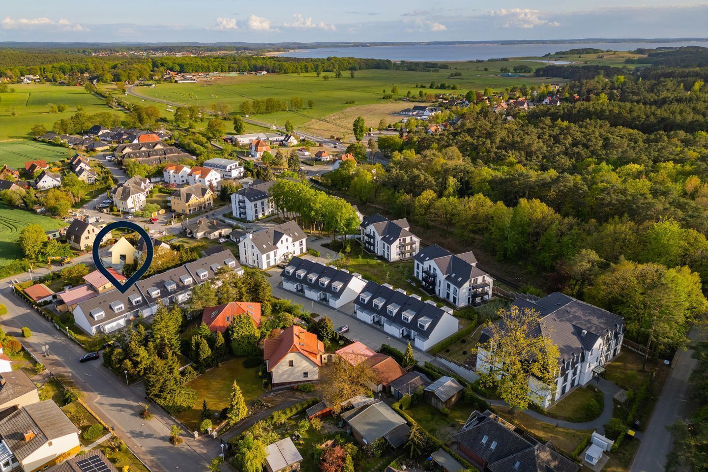 Asuinalue, jossa on sekä kerrostaloja että omakotitaloja, ja jota ympäröi vehreää kasvillisuutta sekä taustalla näkyvä vesistö.
