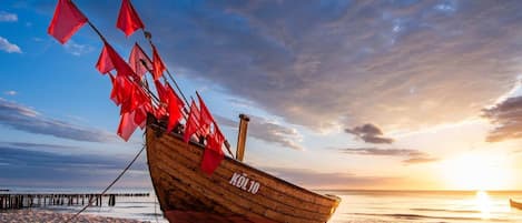 A wooden boat with red flags on a sandy beach at sunset.