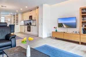 A modern living room with a flat-screen TV, a sofa, a coffee table, and a vase with flowers. - Vacation Home in Nordhorn with a Sun Deck, 2 Bedrooms, and a Beach Chair - (Ostseebad Kölpinsee)