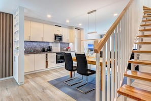 Una cocina moderna con armarios blancos, una escalera de madera y un comedor con dos sillas.