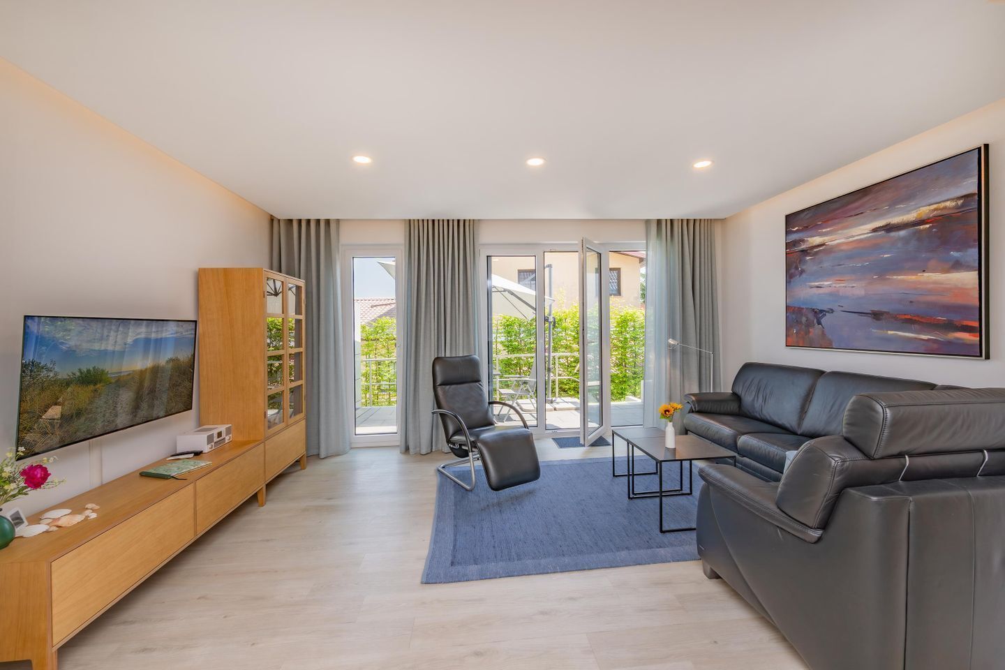A modern living room with a sofa, a TV, a bookshelf, and a view through glass doors to an outdoor area.
