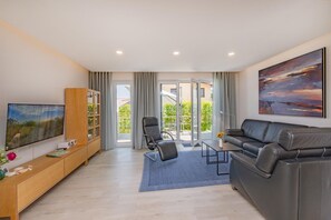 A modern living room with a sofa, a TV, a bookshelf, and a view through glass doors to an outdoor area.