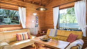 Een gezellig chaletinterieur met houten wanden, een bank, een tafel met drankjes en uitzicht op groen.