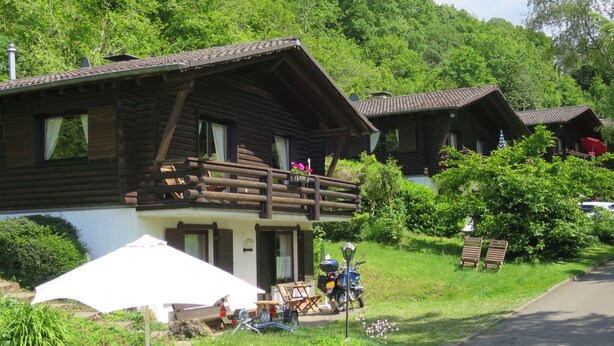Een houten chalet met balkon, omringd door weelderige begroeiing en een heldere lucht.