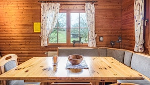 Een houten blokhut van binnen met een eettafel, stoelen en een raam met gordijnen.