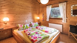 Een slaapkamer in een houten chalet, met een bed, twee wandlampen, een raam met gordijnen en een radiator.
