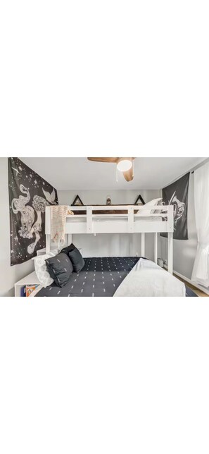 Une chambre avec un lit superposé, un ventilateur de plafond, une tapisserie murale et un lit recouvert d’une couvre-lit à motifs.