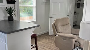 Une cuisine moderne avec un îlot central, un fauteuil en cuir beige et une petite table sur laquelle se trouvent une lampe et des télécommandes.