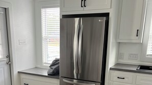 Une cuisine moderne avec des meubles blancs, un réfrigérateur en acier inoxydable et un plancher en bois.