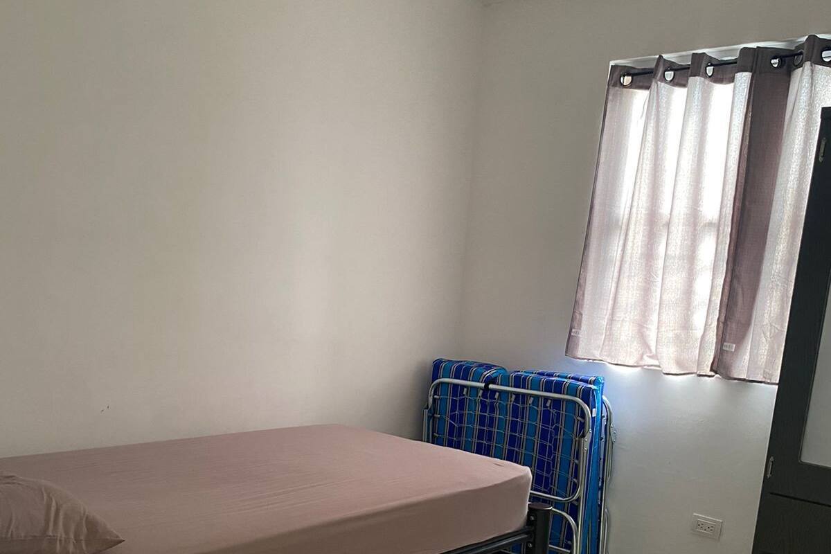 Une petite pièce, peu meublée, avec un lit simple, une petite table et une fenêtre avec des rideaux.