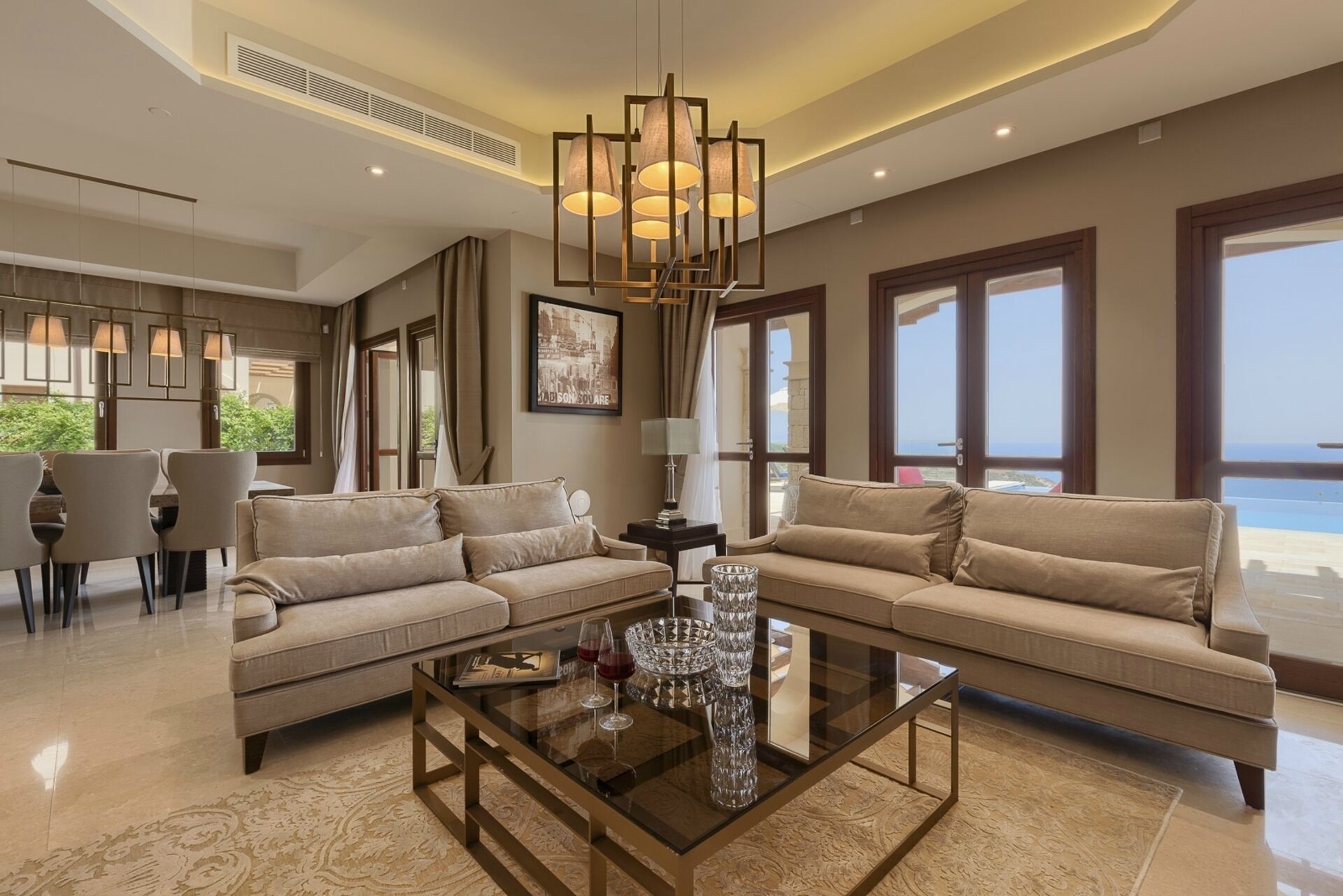 A modern living room with two sofas, a glass coffee table, and a chandelier.