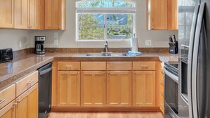 A modern kitchen with wooden cabinets, a stainless steel refrigerator, and a large window with a view of greenery.