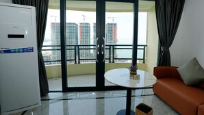 Habitación de hotel con balcón, aire acondicionado blanco, una mesita con un florero y un sofá naranja.
