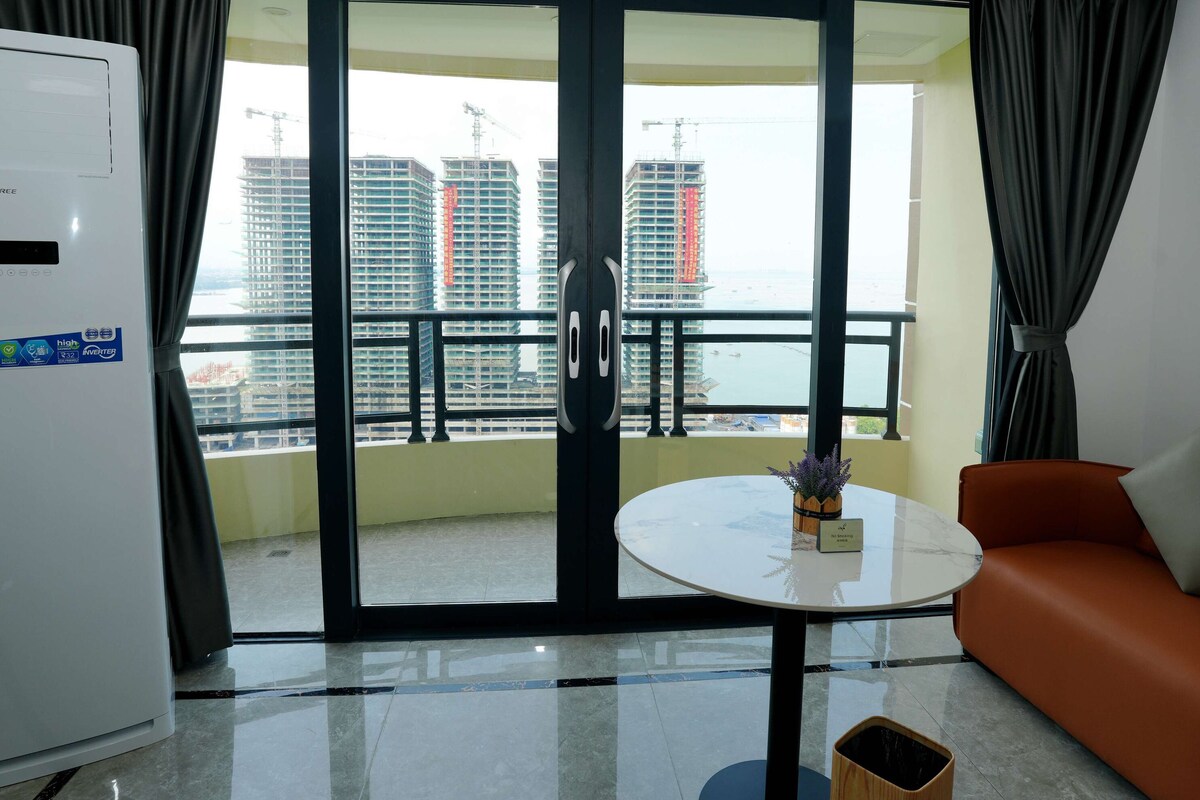 A hotel room with a balcony, a white air conditioner, a small table with a vase, and an orange sofa.