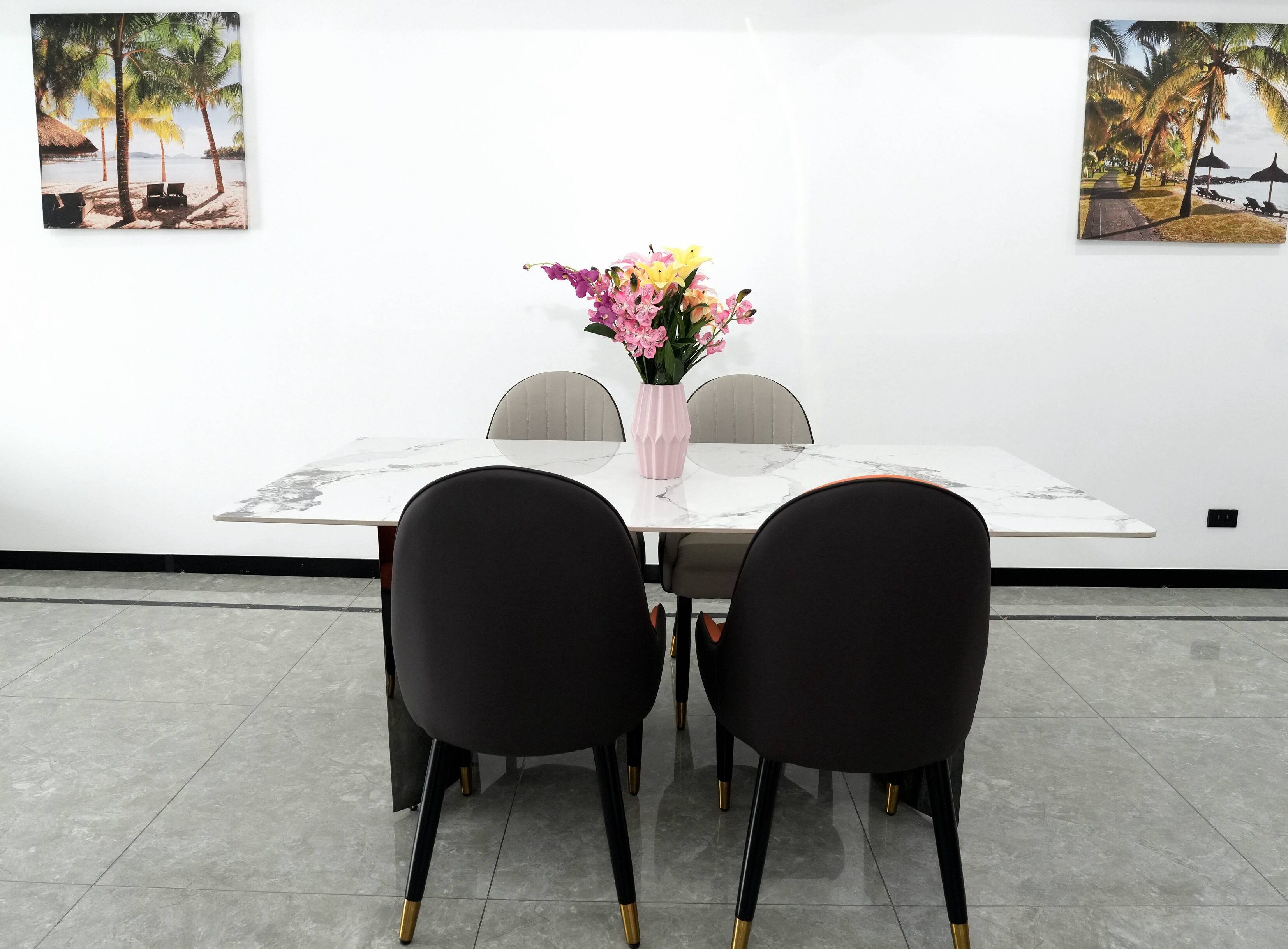 Un comedor con una mesa blanca, sillas negras y un jarrón con flores.