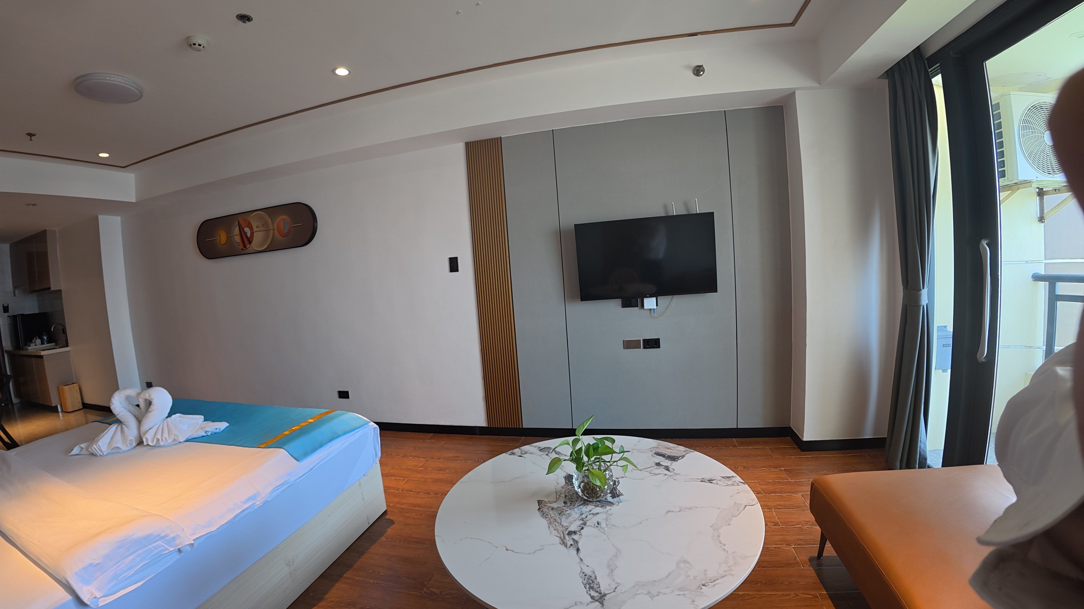 Una habitación de hotel moderna con una cama, un televisor, una mesita de centro de mármol con una planta y vistas al exterior.