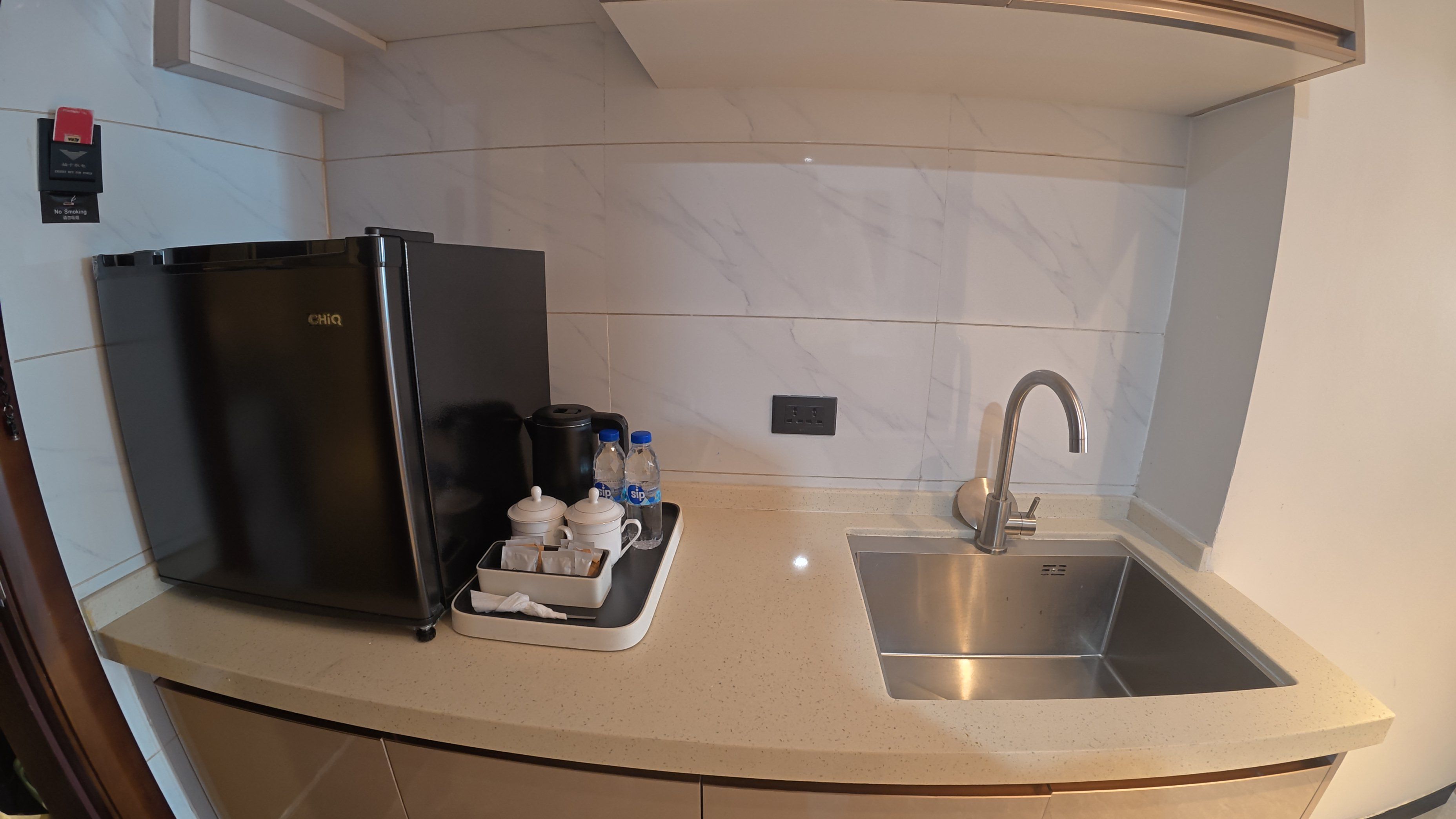 A kitchen with a black refrigerator, a stainless steel sink, and a countertop with a coffee maker and water bottles.