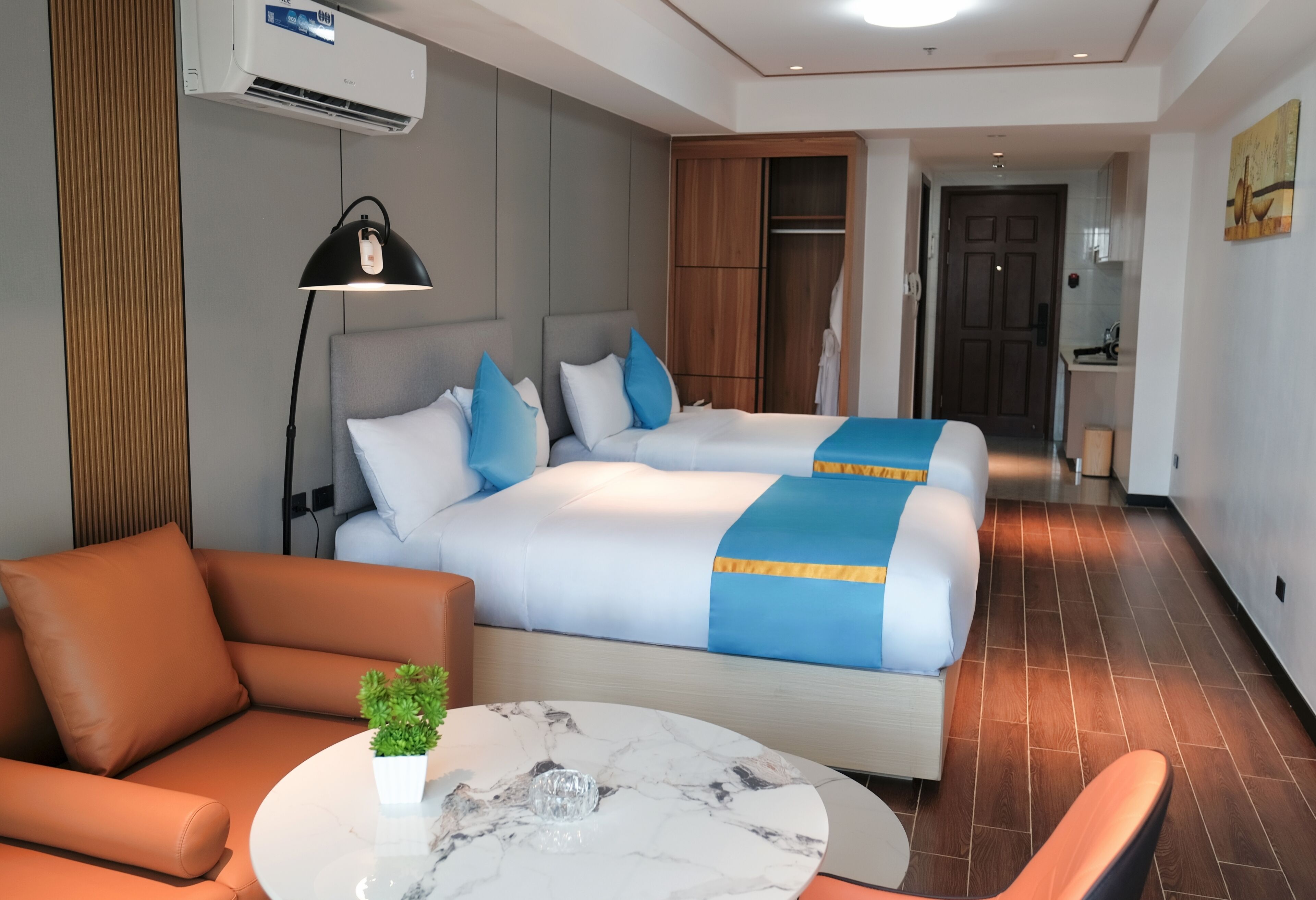 Una habitación de hotel moderna con una cama grande, un sofá, una mesita con una planta y un armario.