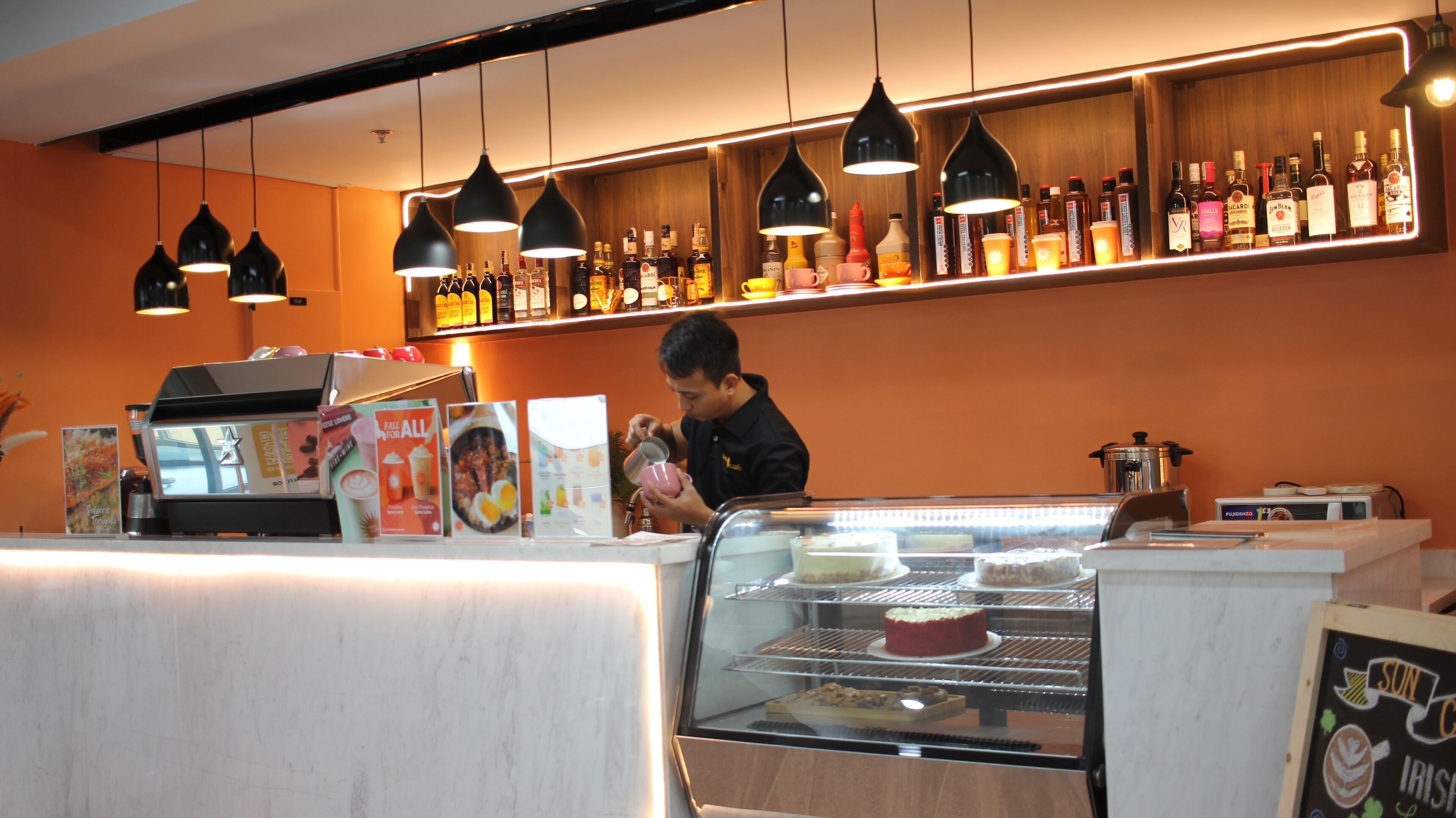 Un espace bar avec un comptoir, une étagère où sont exposées différentes bouteilles, et une personne qui prépare une boisson.