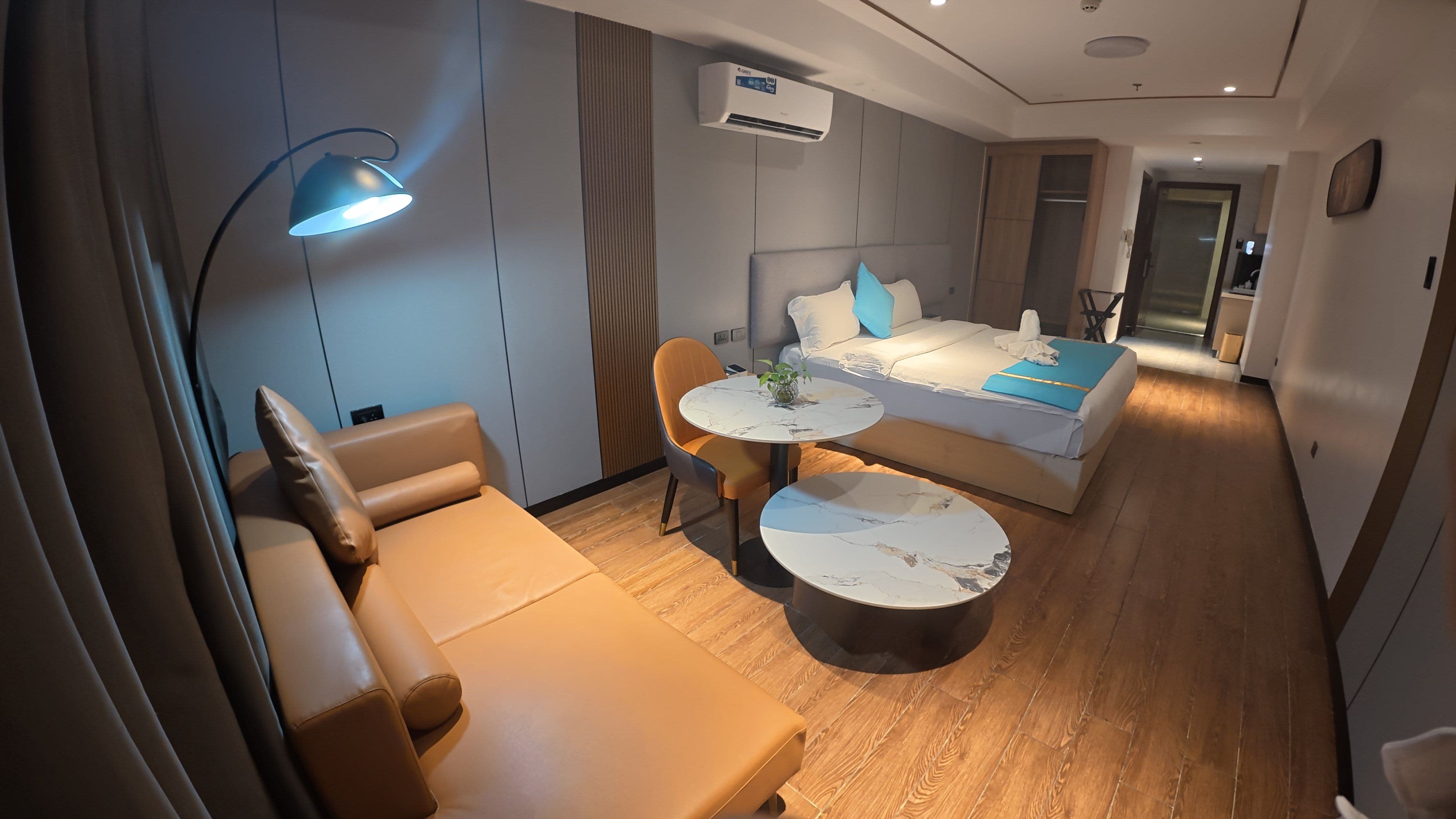 Une chambre d’hôtel moderne, équipée d’un canapé, d’une table ronde, d’un lit agrémenté de touches de couleur bleue et d’un appareil de climatisation.