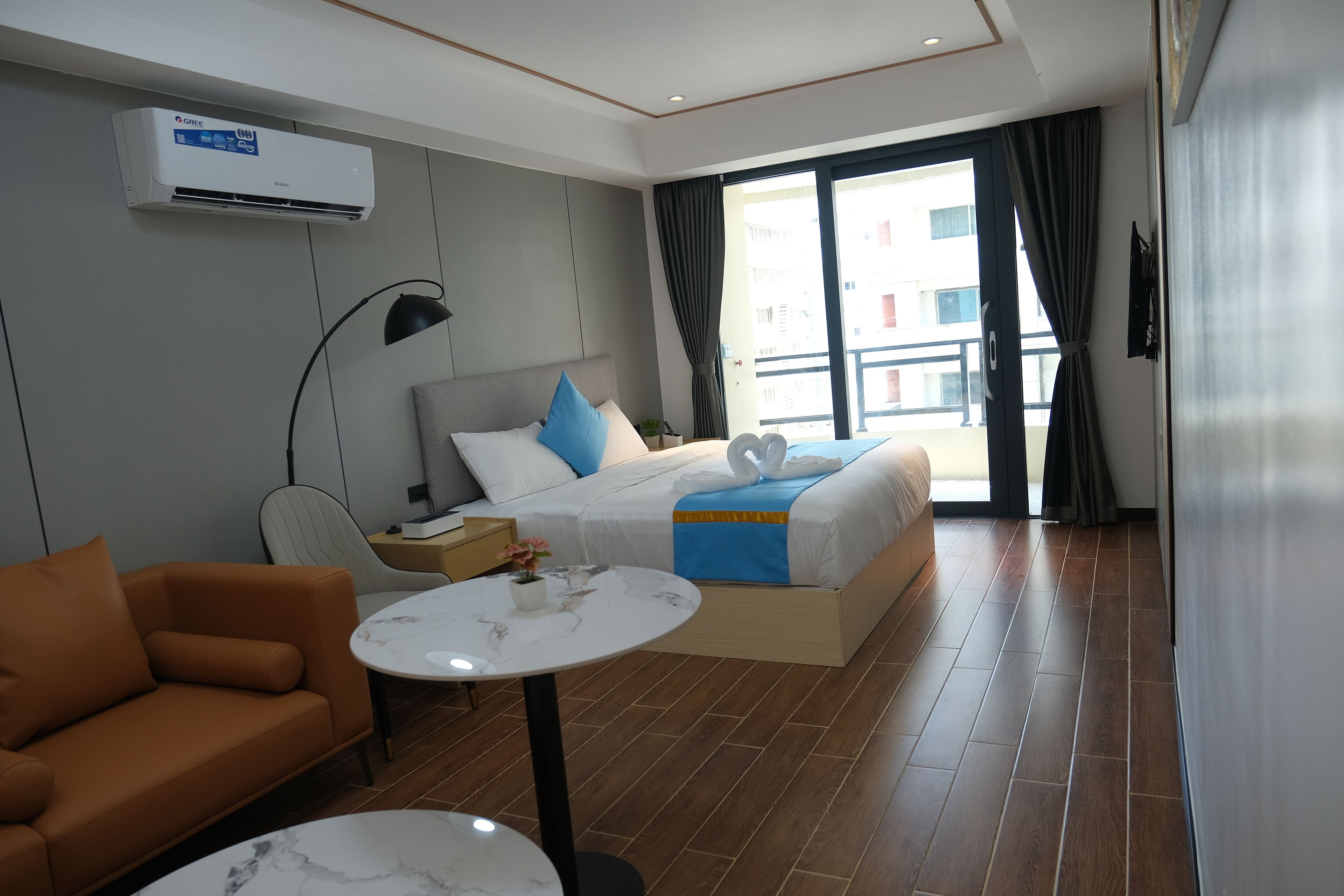 Una habitación de hotel moderna con cama, sofá, una mesita y un ventanal con cortinas.