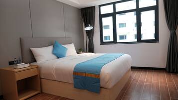 Una habitación de hotel moderna con una cama de madera, una mesita de noche, una ventana con cortinas y vistas a edificios.