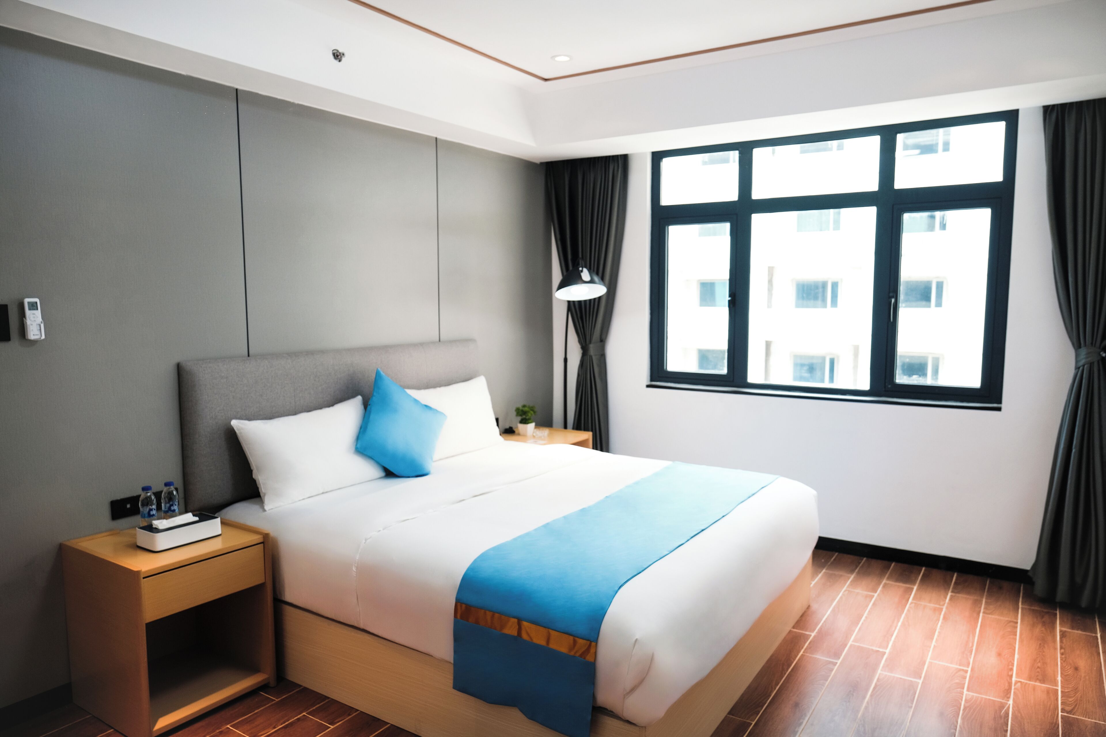 A modern hotel room with a large bed, a nightstand, a lamp, and a window with curtains.