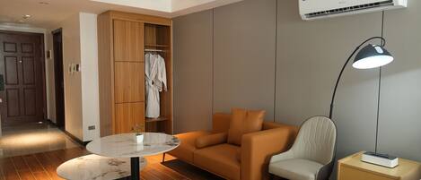 Ein modernes Hotelzimmer mit Holzschrank, einer Couch, einem Sessel, einem kleinen Tisch und einer Nachttischlampe.