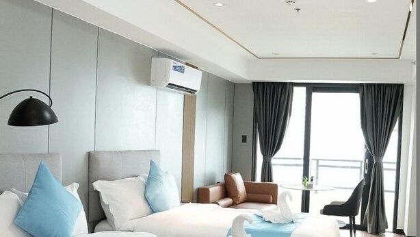 Habitación de hotel con dos camas, un escritorio, una silla y un ventanal con cortinas.