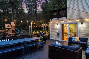 Une terrasse extérieure avec un espace barbecue, des sièges et des guirlandes lumineuses.