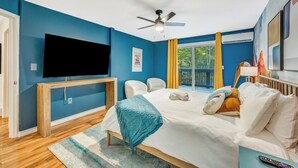 Une chambre moderne avec un grand lit, un téléviseur à écran plat, un ventilateur de plafond et une fenêtre avec des rideaux jaunes.