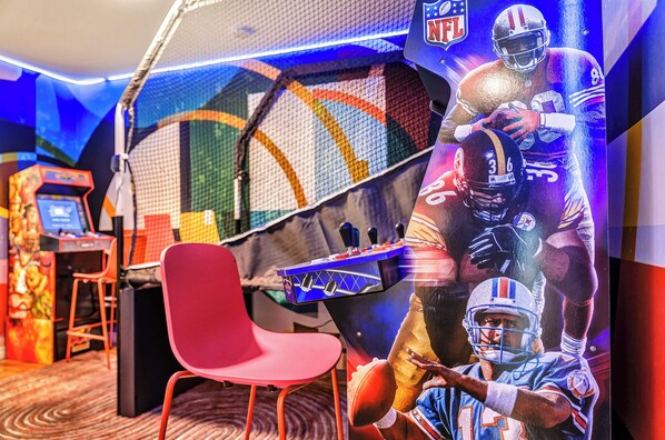 Une pièce avec un fauteuil rouge, un baby-foot et une grande fresque murale sur le thème de la NFL.