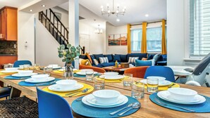 Un coin repas avec une longue table en bois dressée pour le repas, entourée de chaises bleues et jaunes.