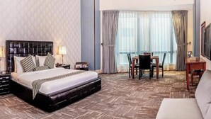 Une chambre d’hôtel avec un grand lit, une table à manger avec des chaises, un canapé et un téléviseur fixé au mur.
