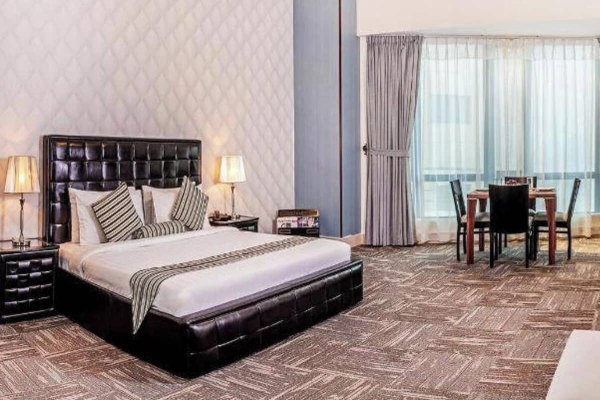 A hotel room with a large bed, a dining table with chairs, a sofa, and a TV mounted on the wall.