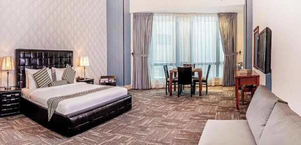 A hotel room with a large bed, a dining table with chairs, a sofa, and a TV mounted on the wall. - Grand Safir Hotel Apartments (Riyadh)
