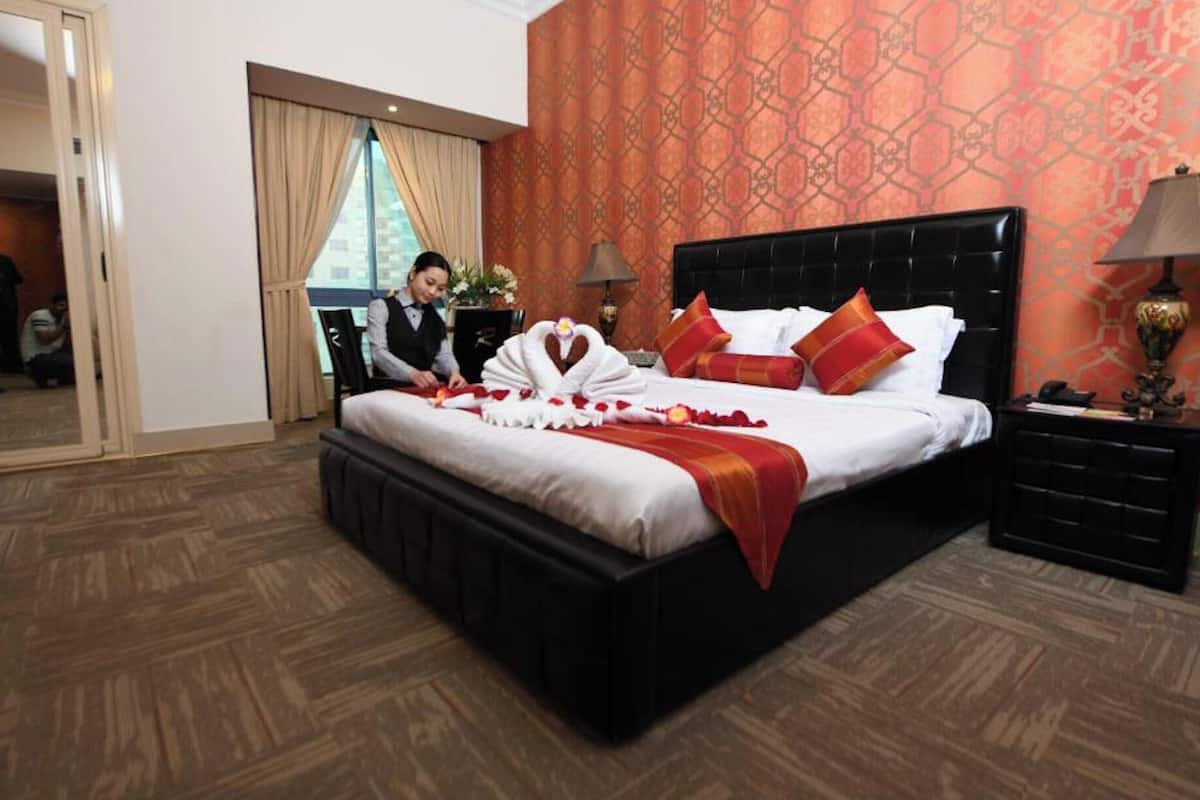 A hotel room with a large bed, red and white bedding, a black headboard, and a wooden floor.