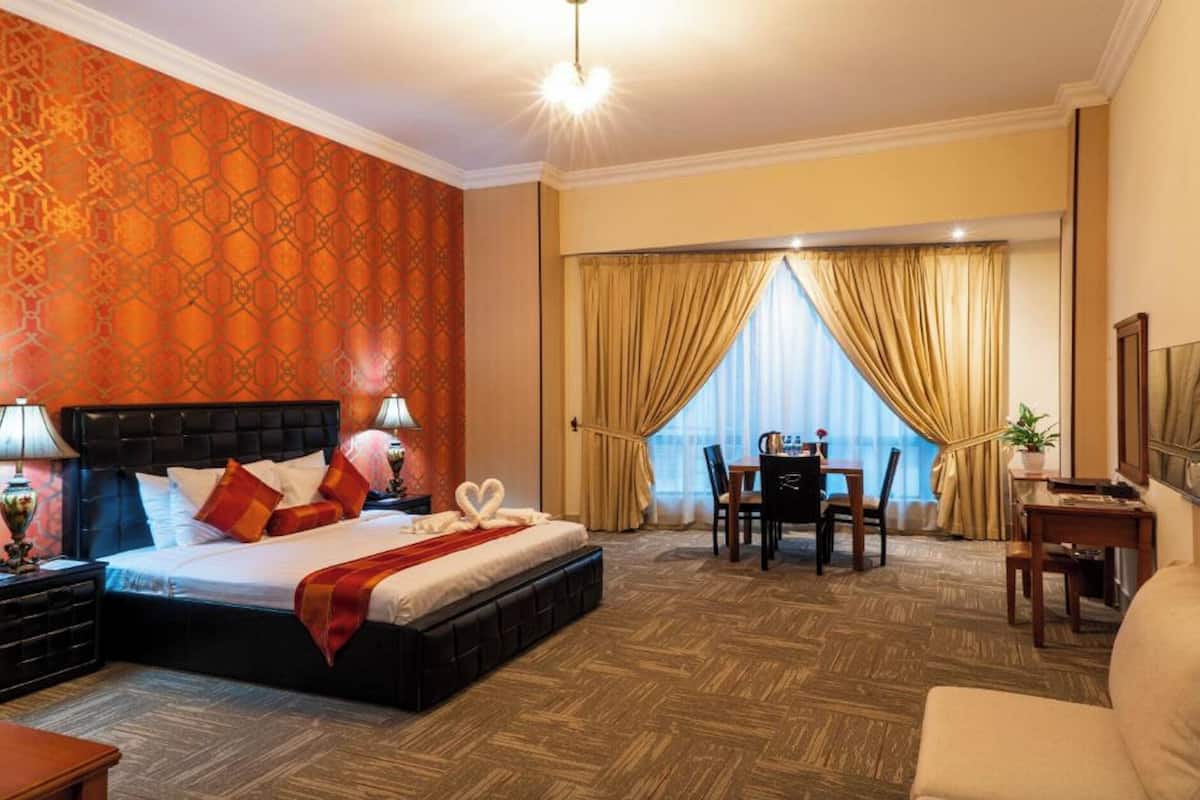 A hotel room with a large bed, a desk, a chair, and a dining table.