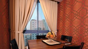 Une chambre d’hôtel avec une table à manger en bois, deux chaises, un panier de fruits et une fenêtre avec des rideaux.