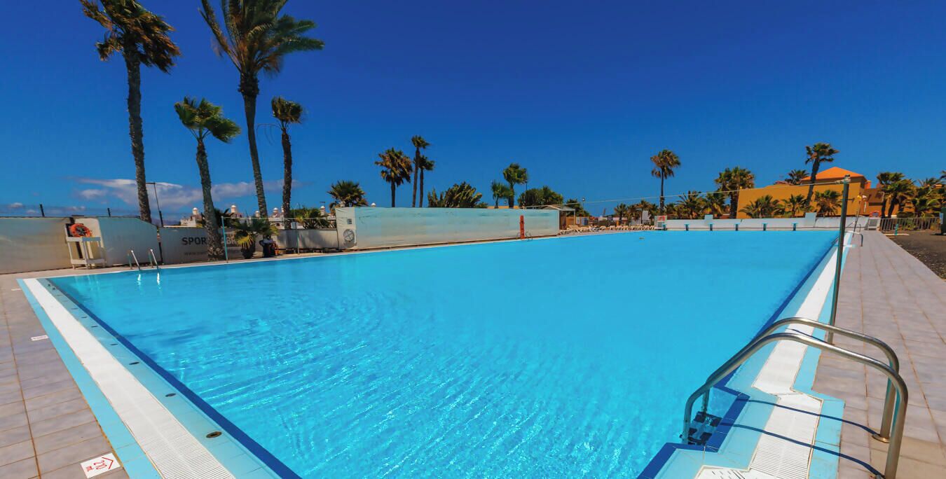 En klar, blå swimmingpool med en metalstige og en flisbelagt terrasse hele vejen rundt.