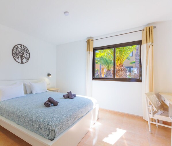 Ein Schlafzimmer mit Bett, Schreibtisch und Fenster mit Blick auf Grünflächen.