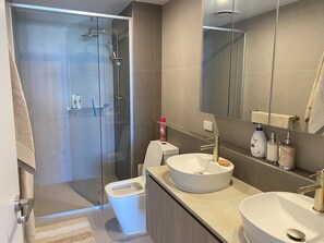 Moderni kylpyhuone, jossa on lasiseinällä varustettu suihku, wc ja kaksi pesuallasta, joiden yläpuolella on peilit.
