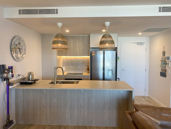 Een moderne keuken met een centraal eiland, roestvrijstalen apparatuur en hangende lampen.