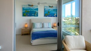A bedroom with a bed, two nightstands, a ceiling fan, and two wall art pieces depicting ocean scenes.