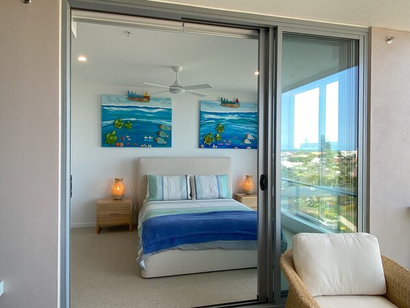 A bedroom with a bed, two nightstands, a ceiling fan, and two wall art pieces depicting ocean scenes. - NEW BEACH Luxury 3B2B, OCEAN VIEWS! 250m to Buddina Beach! (Buddina)