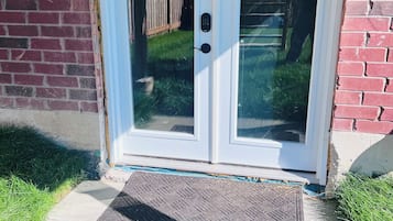 A double glass door with a keypad lock, set in a brick wall, leading to a grassy yard.