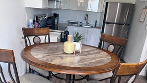 A round wooden dining table with four chairs, a potted plant, and a vase on the table.