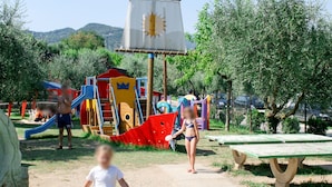 A playground with slides and climbing structures, surrounded by trees and a picnic table. - Vacation home Eden by Interhome (San Felice del Benaco)
