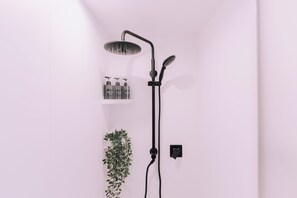 A modern shower with a handheld showerhead, a wall-mounted control panel, and a shelf with toiletries. - Minimalist Loft 601 (Osaka)