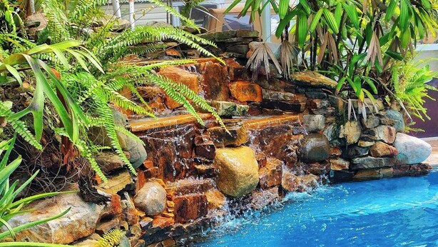 Ein Pool mit einem Steine Wasserfall und üppiger tropischer Bepflanzung.